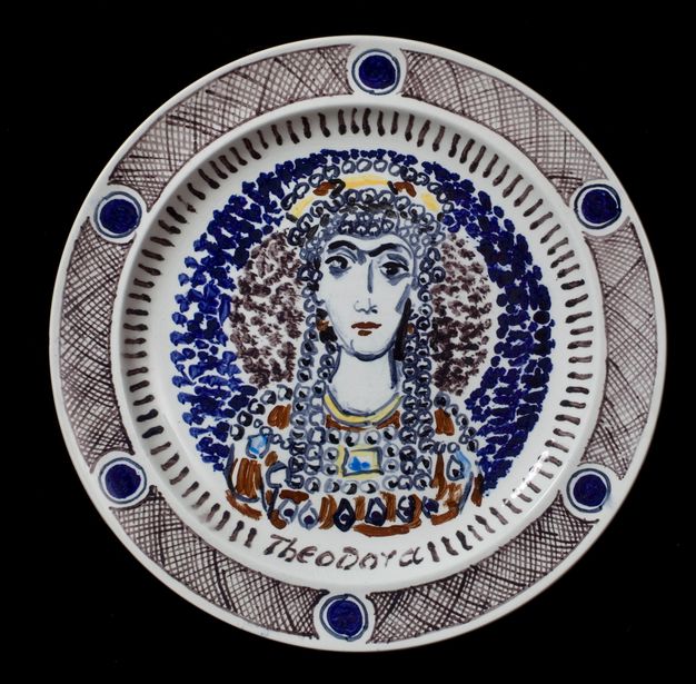 Plate. A woman’s head and shoulders are sketchily painted mostly in shades of blue and brown and with a few touches yellow. Circles over her head and down the sides of her face suggest a headdress and other jewelry. Her name is painted below, \“Theodora\”.