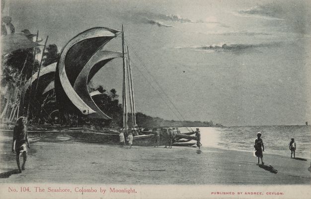 Black and white photograph. In this image reproduced on a postcard, moonlight warms the sky, and it reflects off water below. The sails of a sailboat puff full in the wind even though the boat is pulled onto a flat beach to our left.